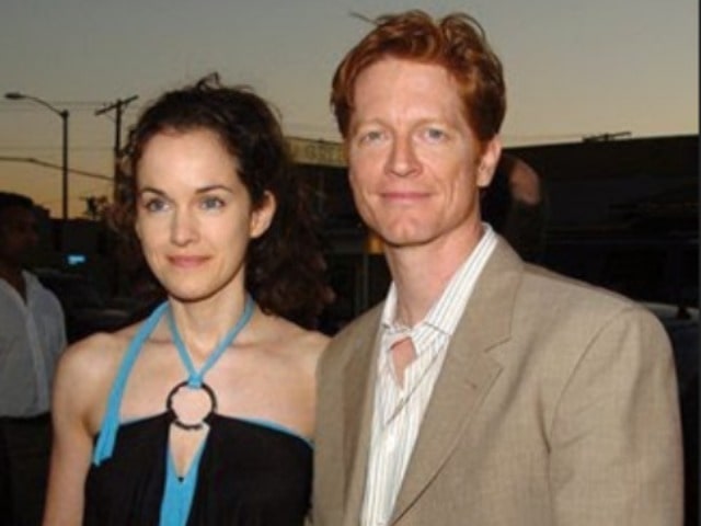 Eric is wearing a light brown coat with white shirt.